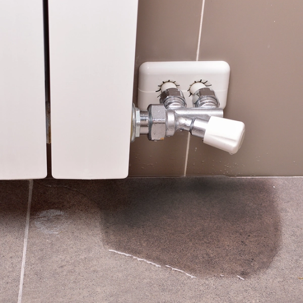 Dépannage d'urgence plomberie : fuite d'eau au niveau du robinet d'un radiateur à eau, avec une flaque au sol
