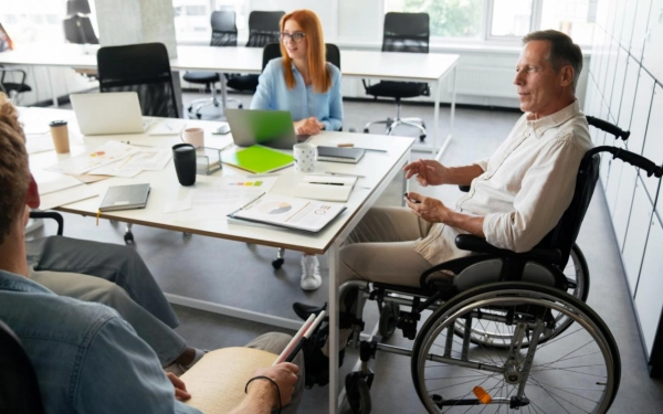 Réunion de travail avec un participant en fauteuil dans des bureaux aménagés PMR