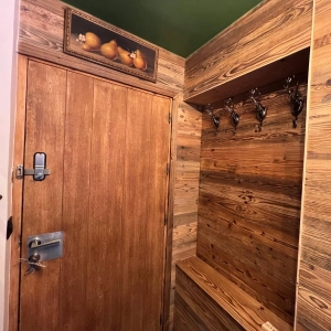 Entrée rénovée de chalet de montagne, tout en bois, avec niche intégrée dans le mur comprenant des porte-manteaux en fer