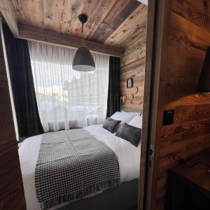 Rénovation de chambre de chalet de montagne, revêtement des murs en bois ancien, porte à galandage en épicéa, vue sur l'intérieur de la chambre avec lit deux personnes prêt à l'emploi