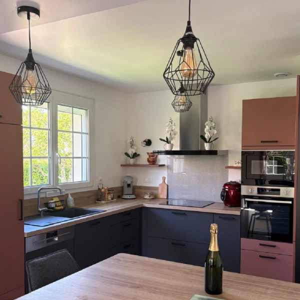Cuisine aménagée et équipée avec façades de meuble noires et corail. Bouteille de champagne posée au premier plan sur la table.