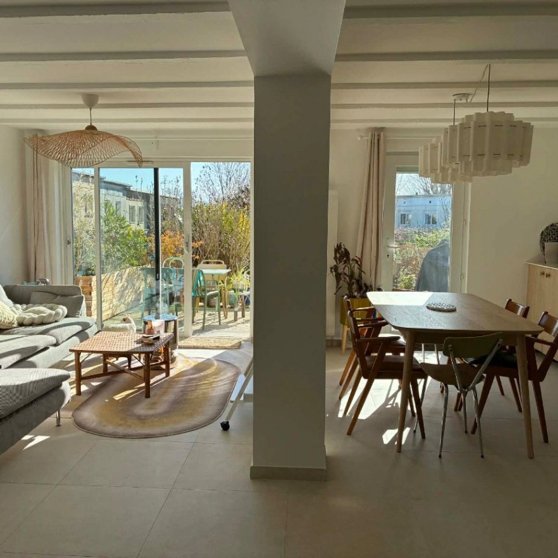 Vue sur pièce de vie principale : cuisine, salle à manger et salon avec poteau central. Porte et baies vitrées en arrière-plan.