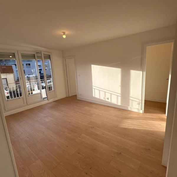 Appartement rénové à Caen, finitions soignées. Vue du salon peint en blanc, parquet posé, baie vitrée et balcon