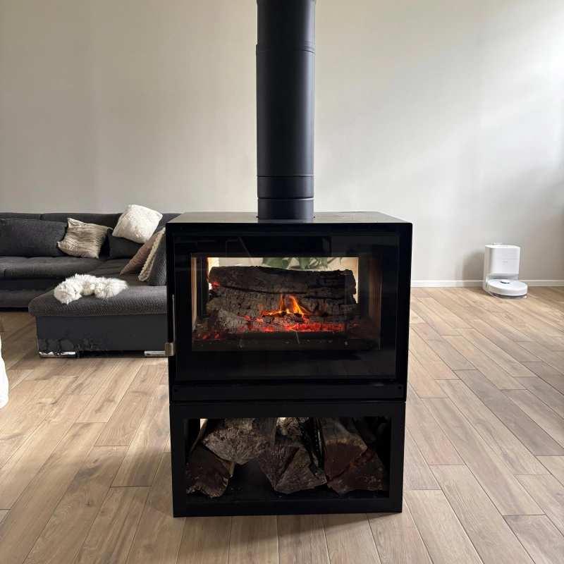 Photo du poêle à double face avec un feu d'allumé, placé au centre de la pièce