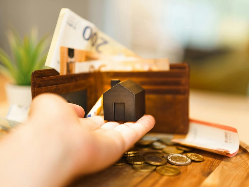 Petite maison posée dans la main tendue d'une personne avec des billets en arrière-plan