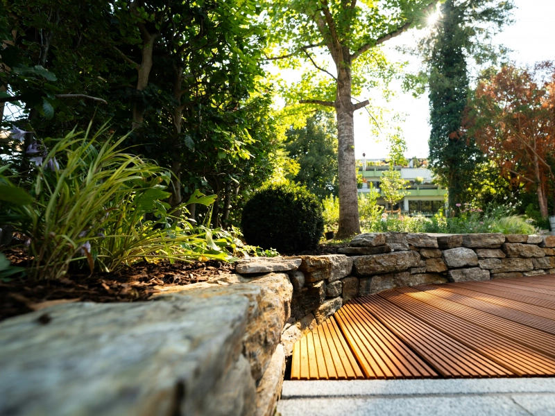 Extérieur aménagé avec muret en pierres, terrasse en bois et ornements végétaux
