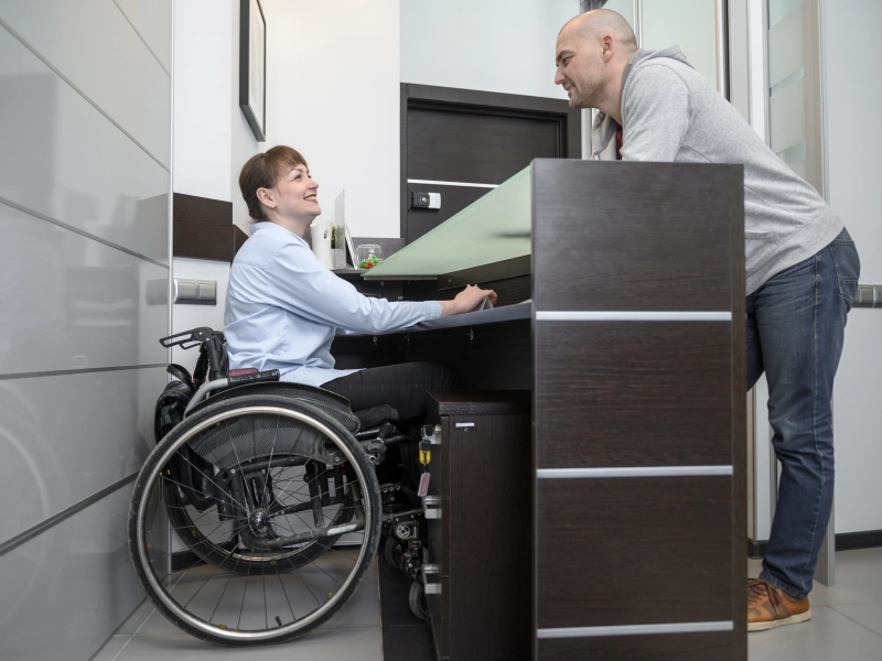 Femme en fauteuil travaillant à l'accueil d'une structure, avec un comptoir adapté à son handicap